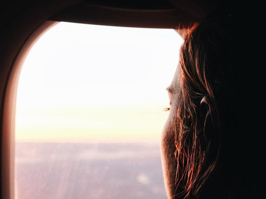 A view out of an aircraft window at dusk, a passenger's silhouette against the light.